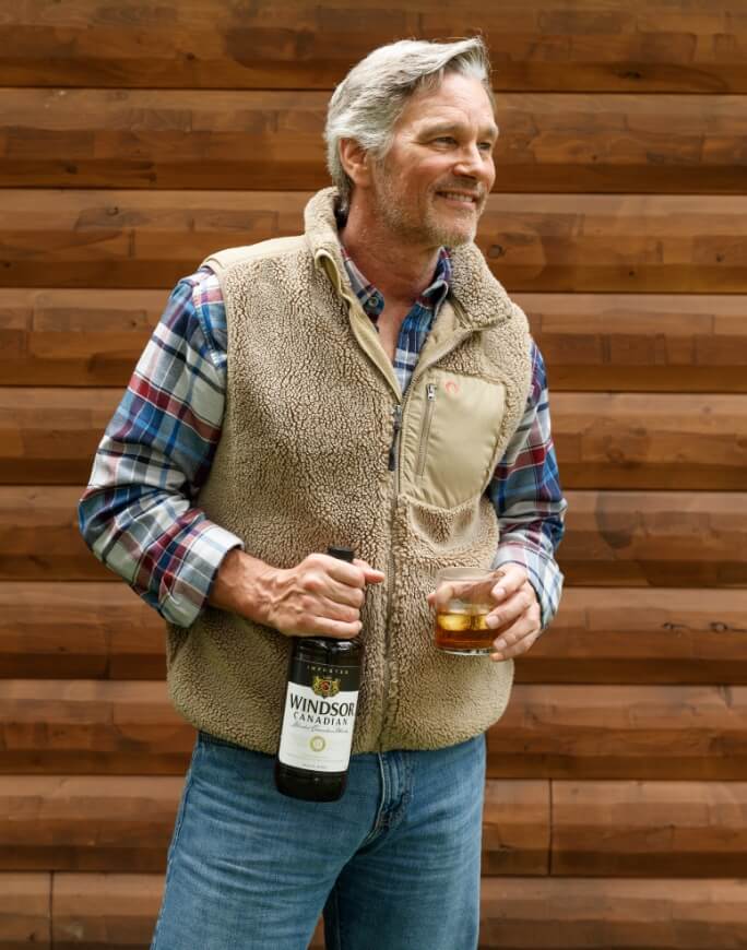 Man holding a glass and a bottle of windsor canadian whiskey